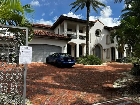 A City of Miami code-violation notice taped to the gate of the raided house, with a blue BMW still in the driveway