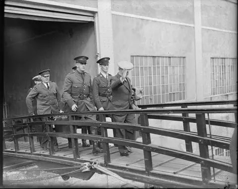 Ponzi waves his cap as immigration officers walk him up the gangplank of the SS Vulcania